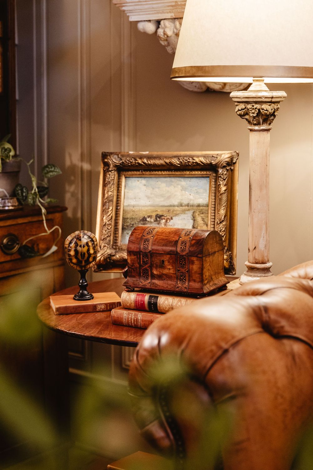 A small vintage chest sits on an end table with a vintage lamp beside a leather couch.