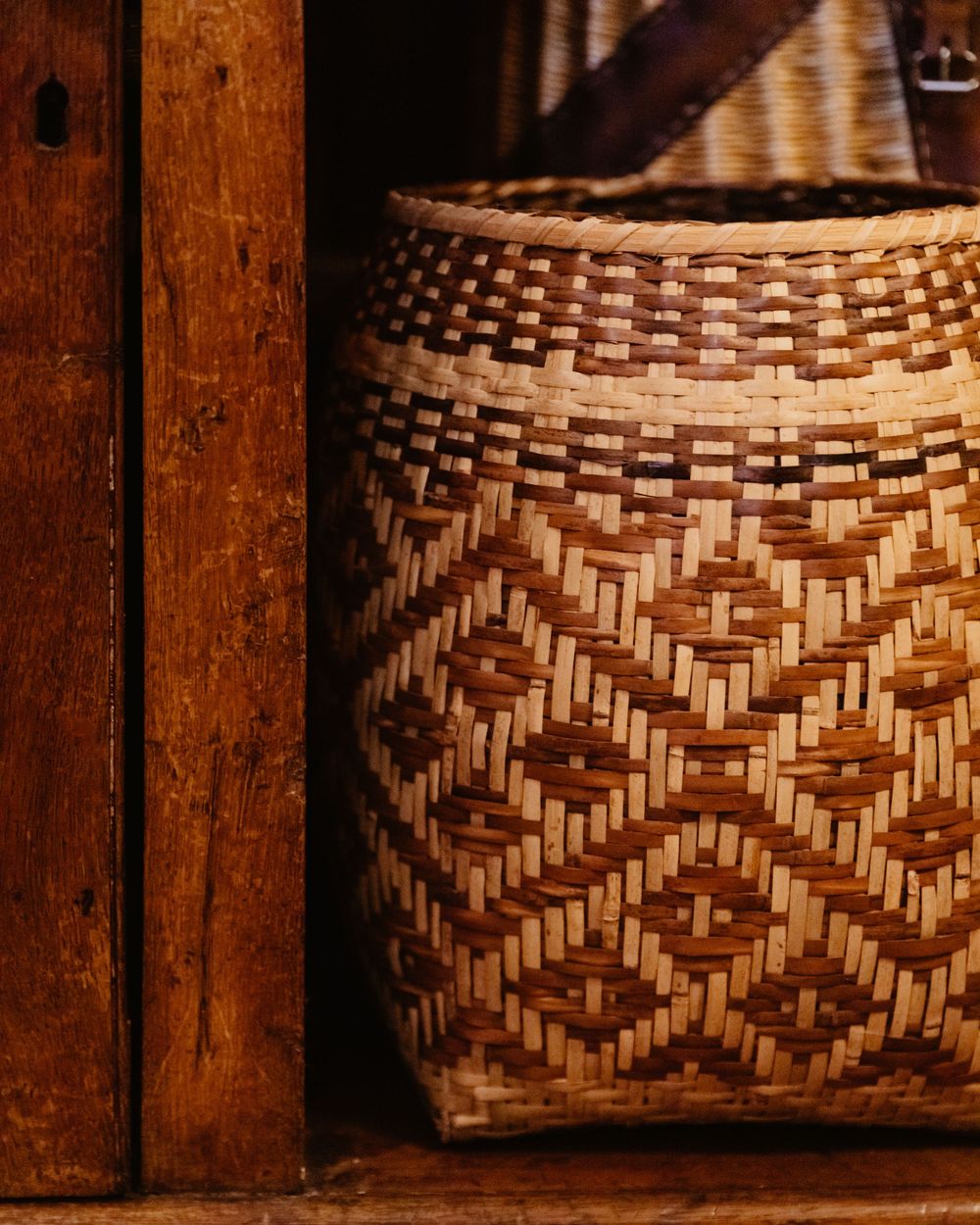 A close-up photo diamond-patterned woven basket is sitting on a lower shelf of a cabinet.