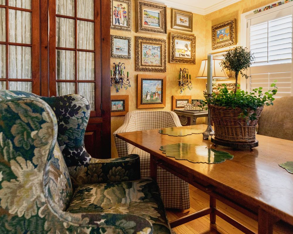 Colorful yellow dining room wall with folk art hung gallery style with a table and a floral green armchair