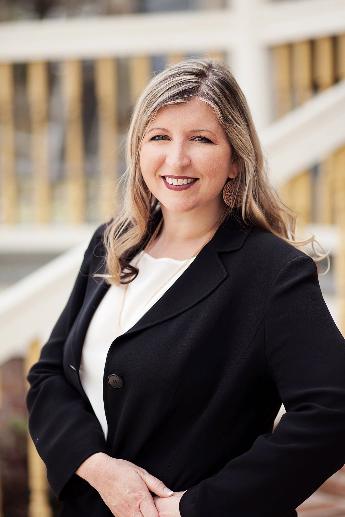 Professional headshots of a person wearing a black blazer and white top against a blurred background.