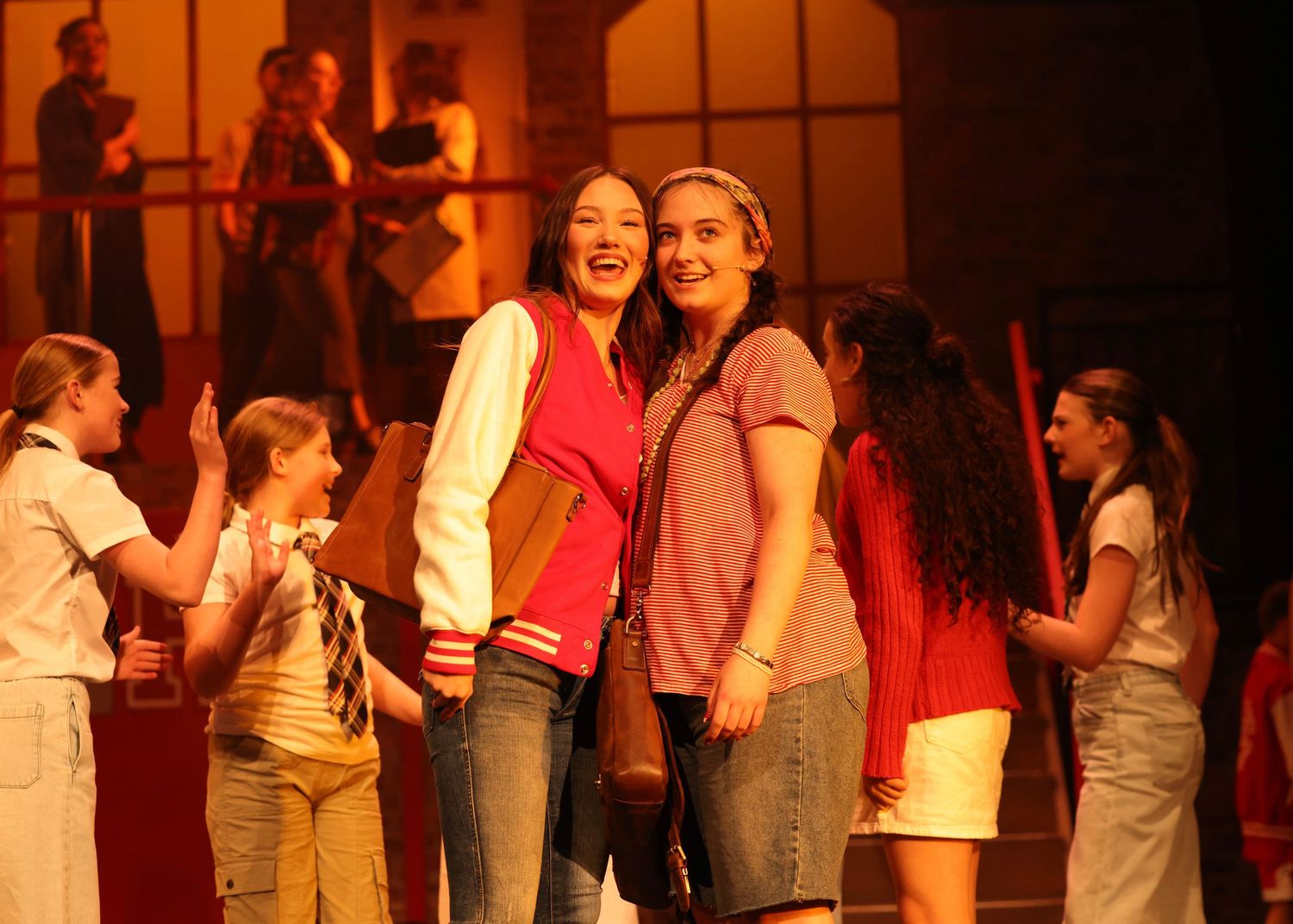 Performers in white shirts and casual attire stand together on stage during a theatrical production with warm lighting.