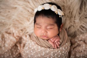 Peaceful newborn portrait with cream floral headband against textured beige backdrop.