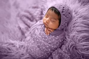 Sleeping newborn on plush purple textured blanket with delicate details.
