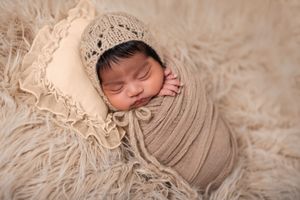 Sleeping newborn wrapped in neutral beige fabric on soft textured backdrop.