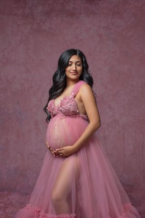 Maternity portraits in flowing pink tulle gown against burgundy studio backdrop.