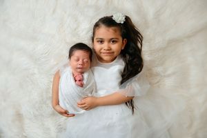 Baby and child on white fluffy blanket during professional photo session.