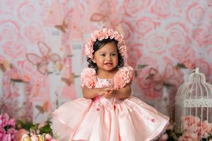 Soft pink backdrop with floral patterns and vintage birdcage creates a delicate setting.