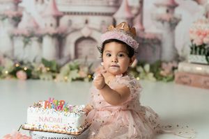 Birthday celebration with pink castle backdrop, balloons, and decorated cake on display.