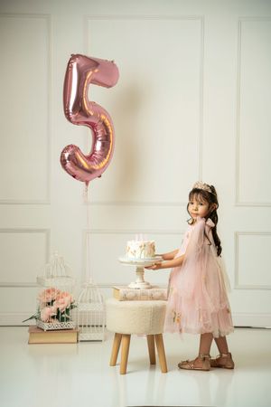 Birthday celebration setup with pink number 5 balloon, white furniture, and delicate pink decor.