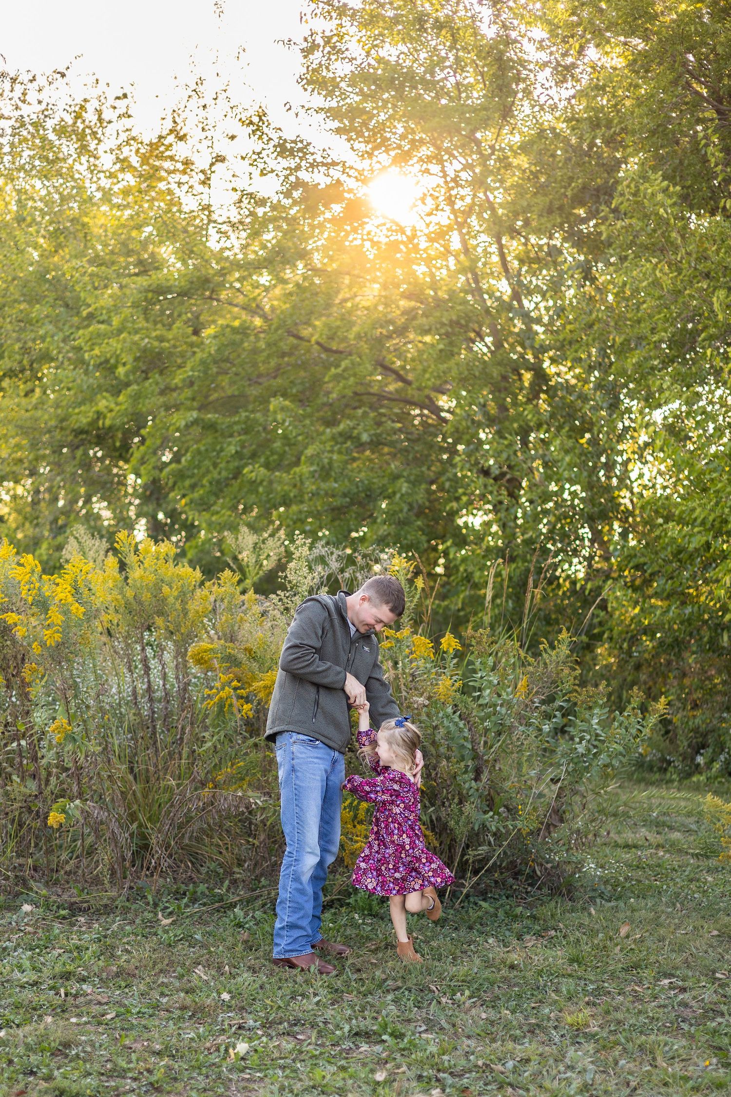 Springfield IL Photographer captures a dad twirling his daughter in front of trees and wildflowers at Centennial Park, Springfield, IL