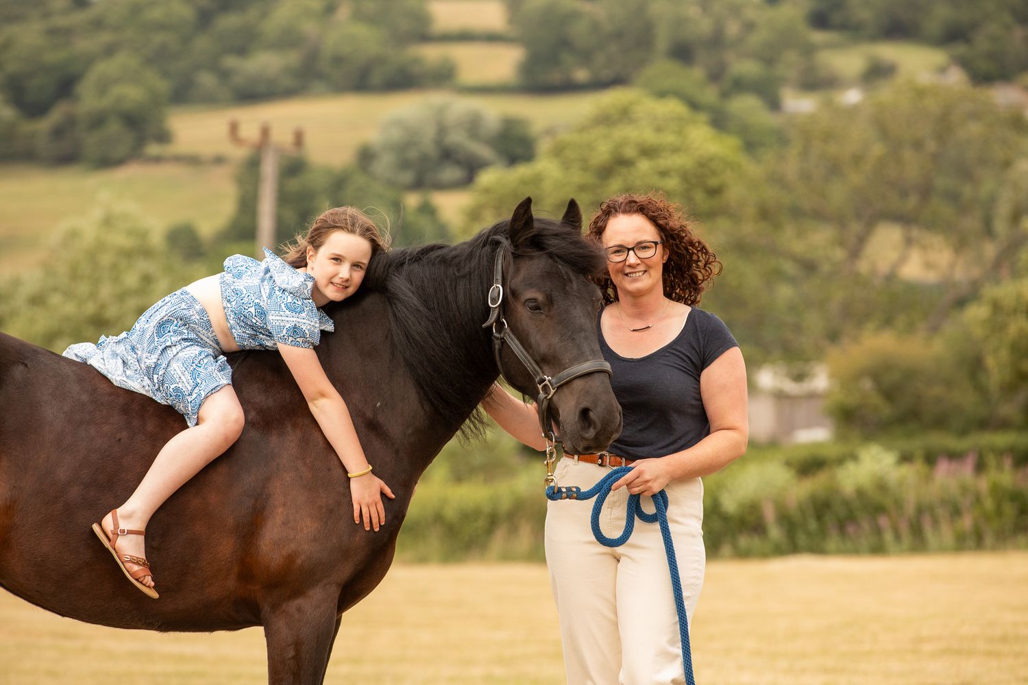 Two joyful riders lean over a white horse's back in a sun-drenched field at golden hour.