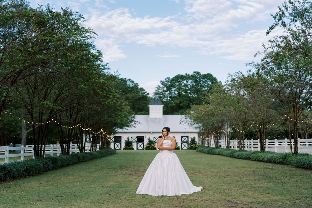 A white wedding gown on display against a scenic backdrop of a white barn and green lawn with trees.