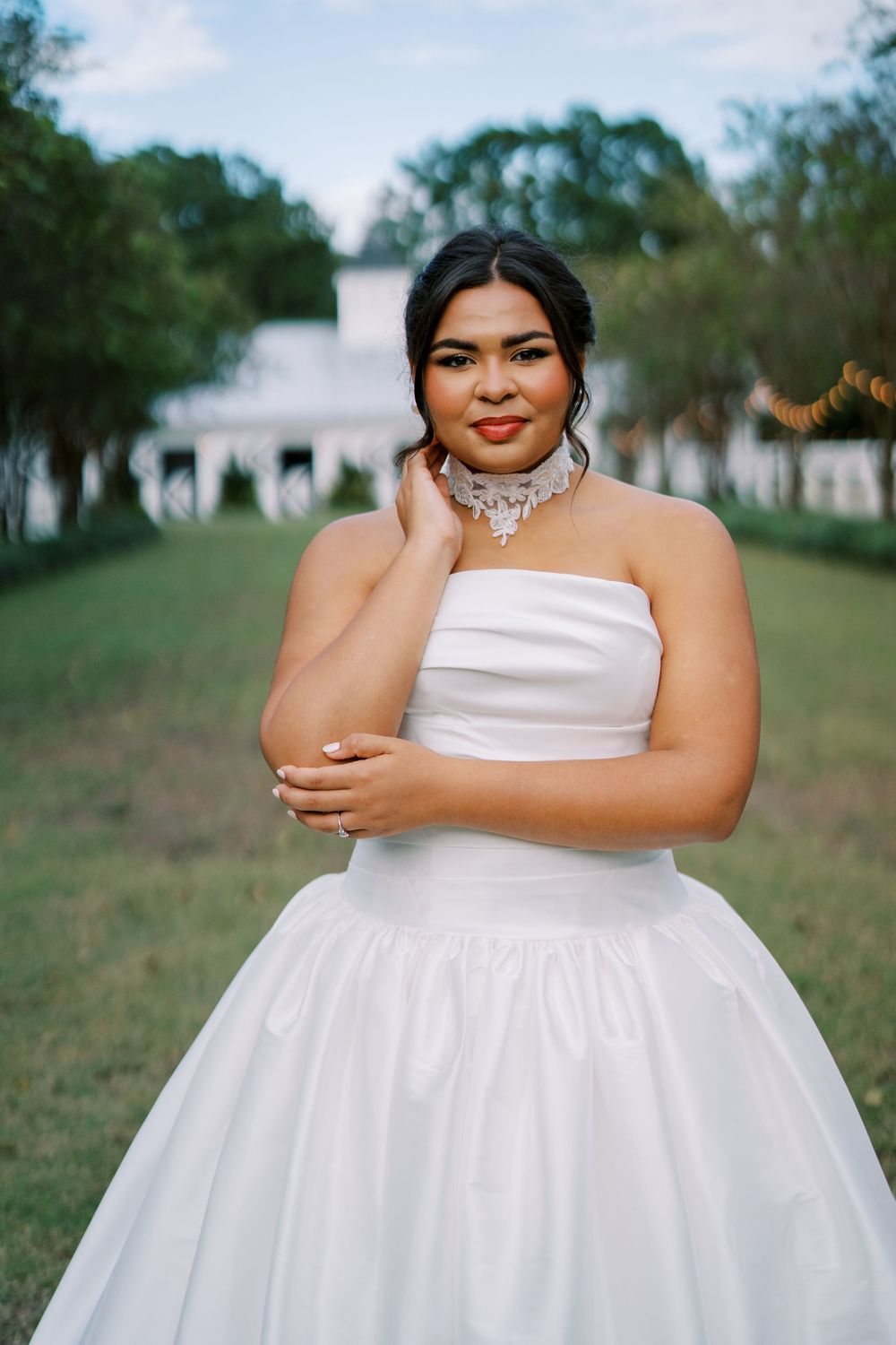 Full-length bridal portrait in a flowing white strapless gown against a natural outdoor setting.