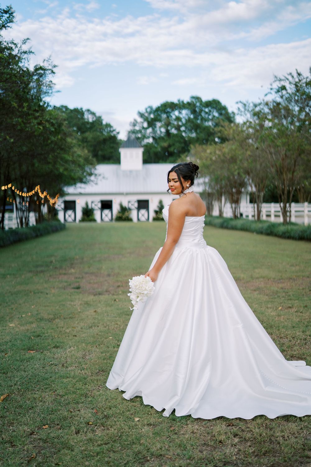 Flowing white wedding dress with dramatic train photographed on grassy lawn with buildings in background.