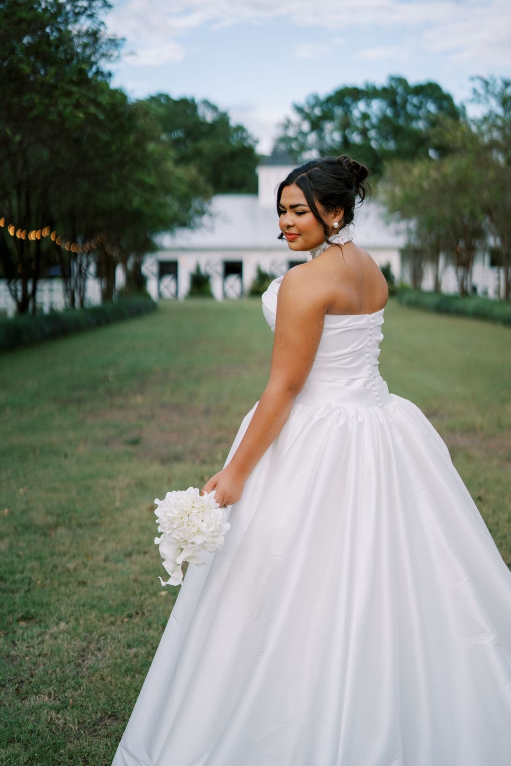 A flowing white ball gown wedding dress photographed in an outdoor garden setting with string lights.