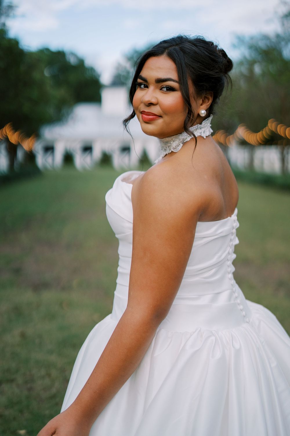 A bride wearing a strapless white wedding gown poses in a lush garden setting.