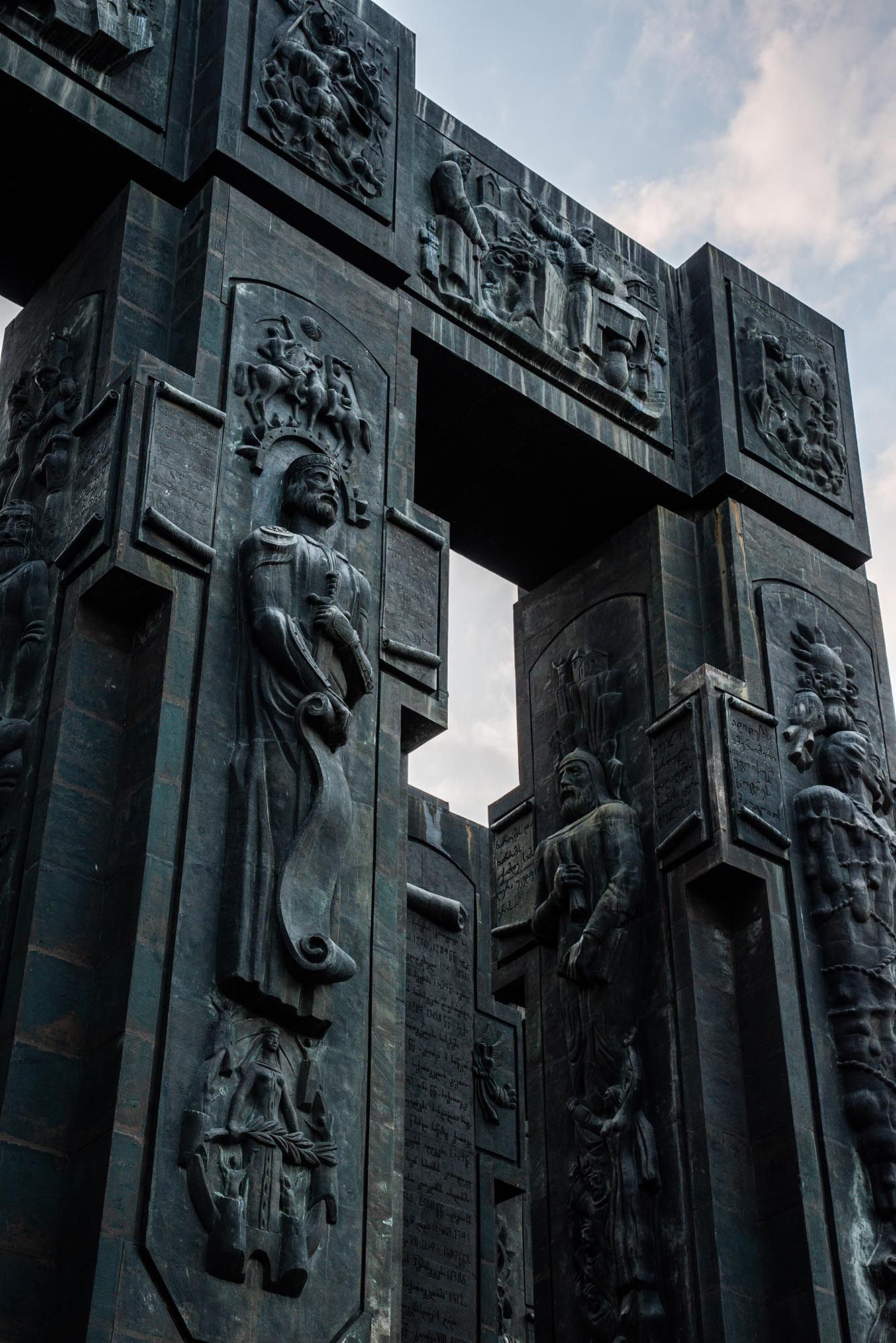 Dramatic architectural relief sculptures on a stone building facade showing figures and geometric patterns in low light.