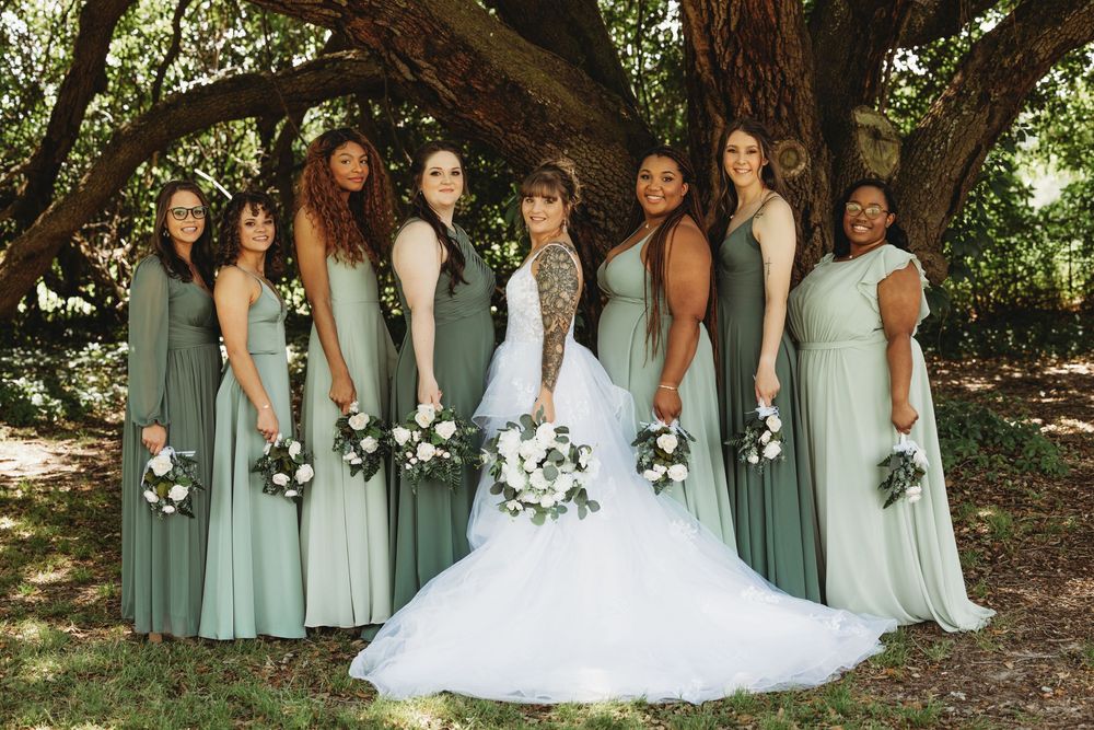 Wedding party in sage green bridesmaid dresses posed outdoors with white bouquets.