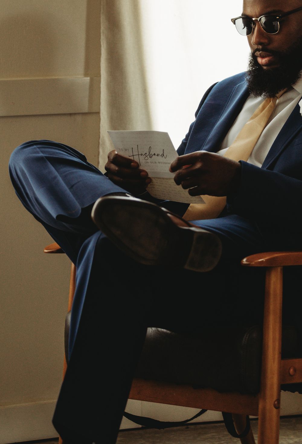 Person in navy suit relaxes in armchair during wedding preparations.