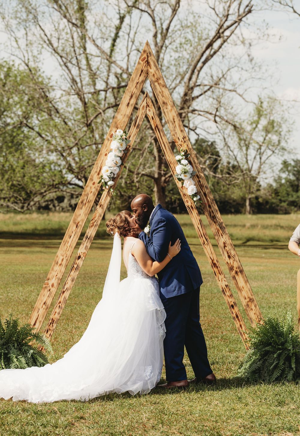 Wedding couple poses under rustic wooden ladder arch in outdoor garden setting.