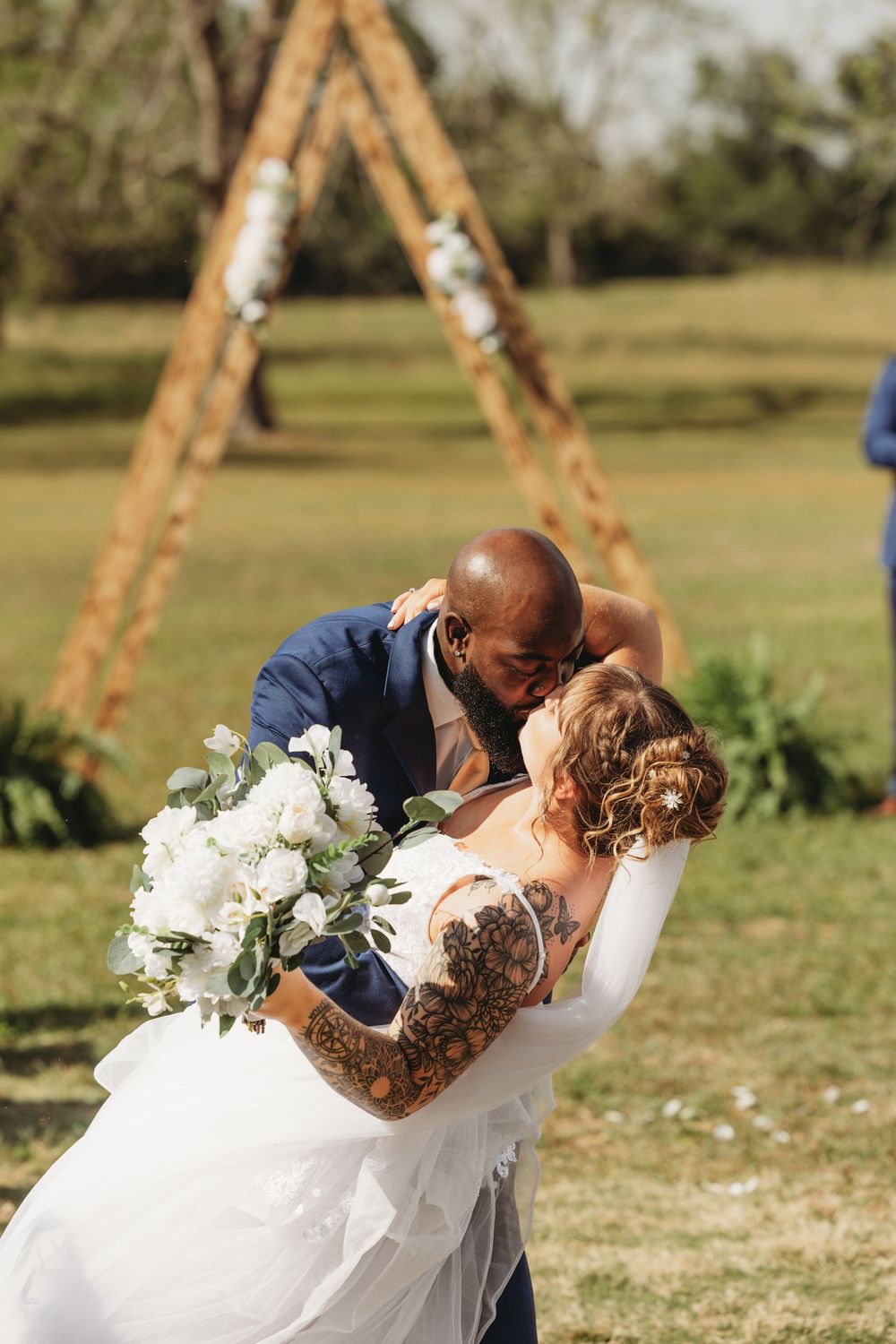Romantic wedding dip pose under wooden arch decorated with greenery.