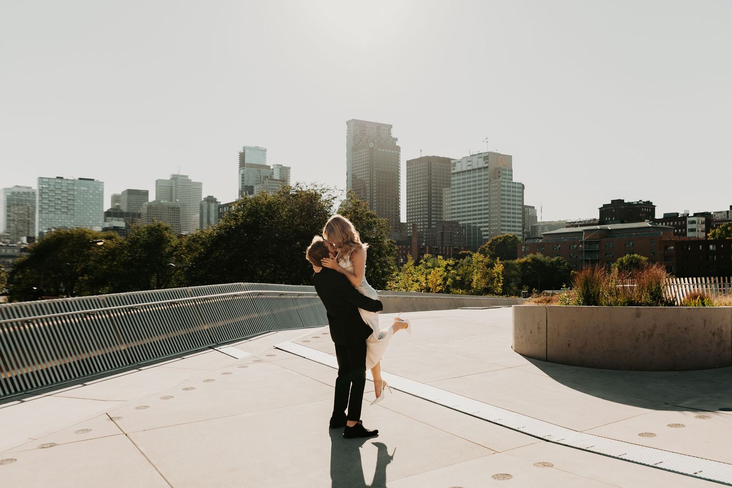 Two people embrace on a rooftop with the Minneapolis skyline visible in the background during golden hour.