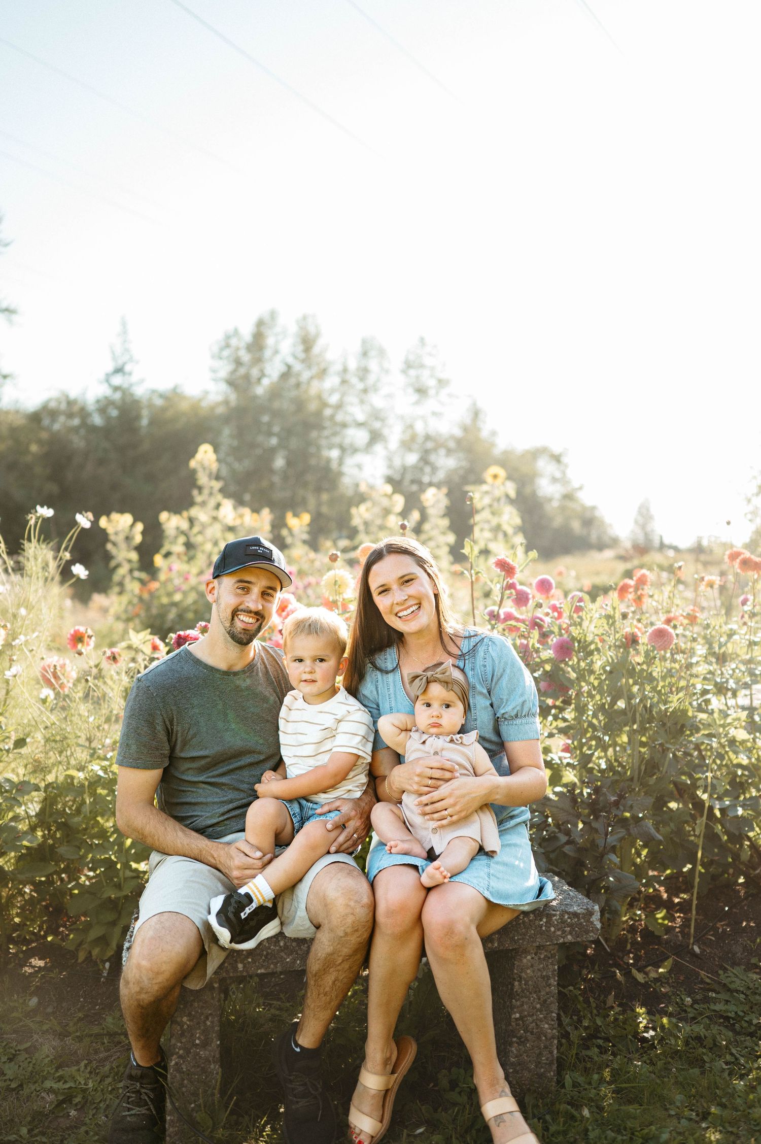 A family sits together on a bench surrounded by blooming flowers in a garden during golden hour.