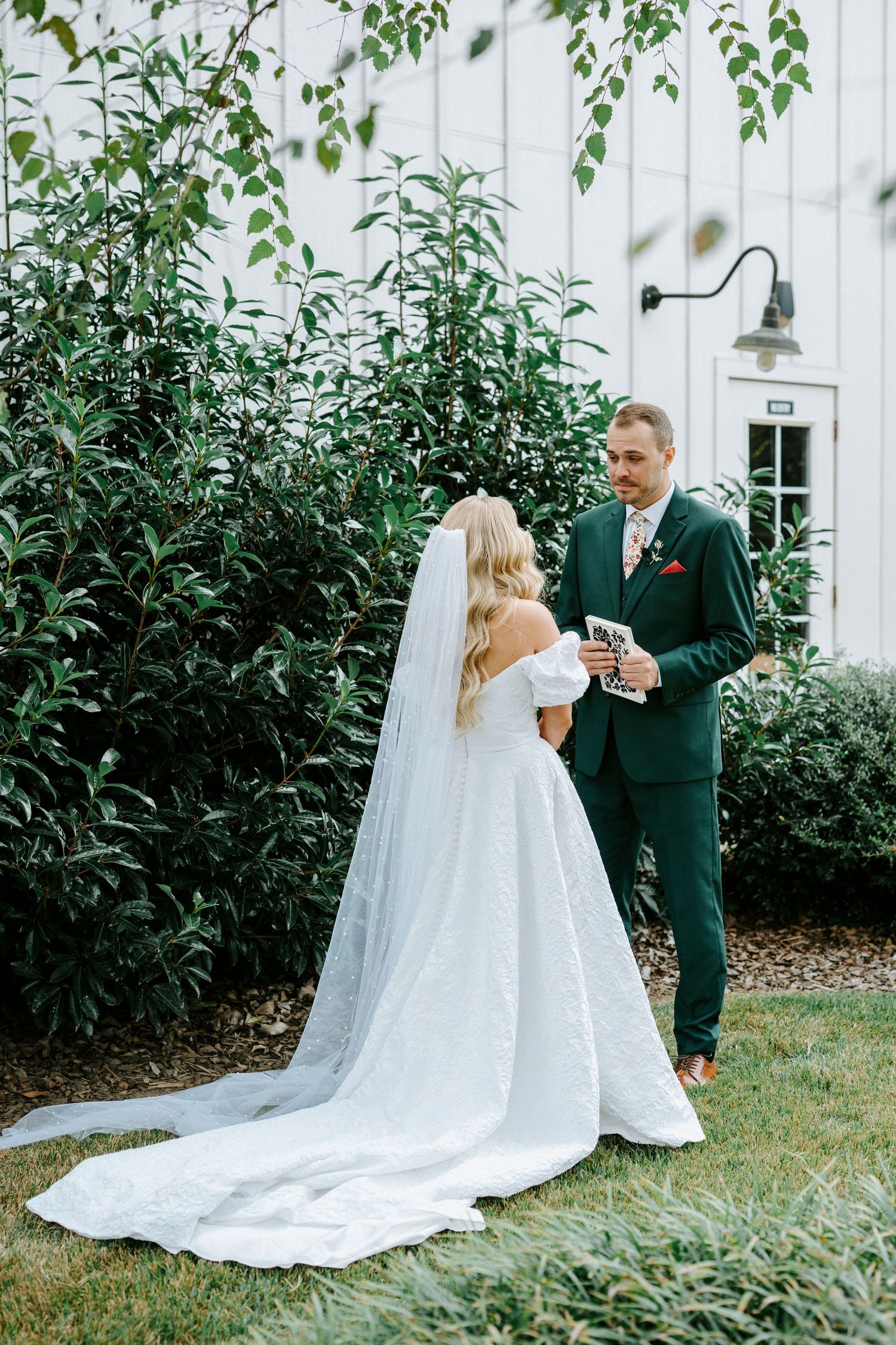 A couple shares an intimate moment in a garden setting with a white church backdrop and flowing wedding dress train.
