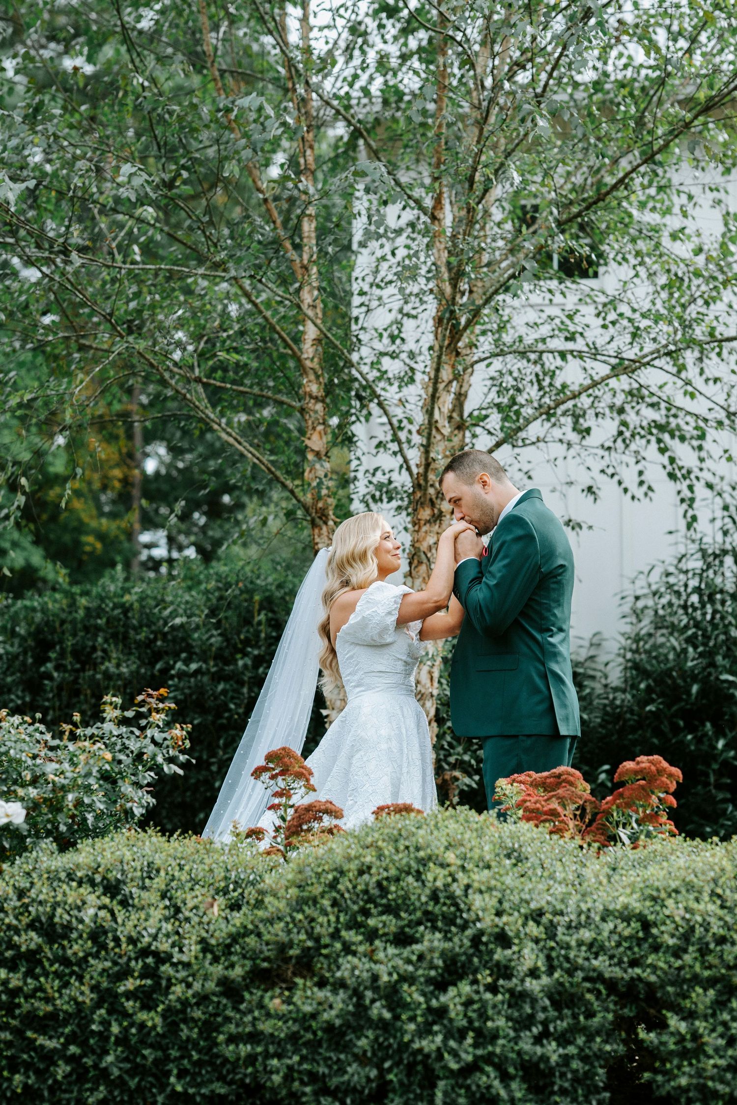 A couple shares an intimate moment during their wedding ceremony surrounded by lush greenery and autumn flowers.