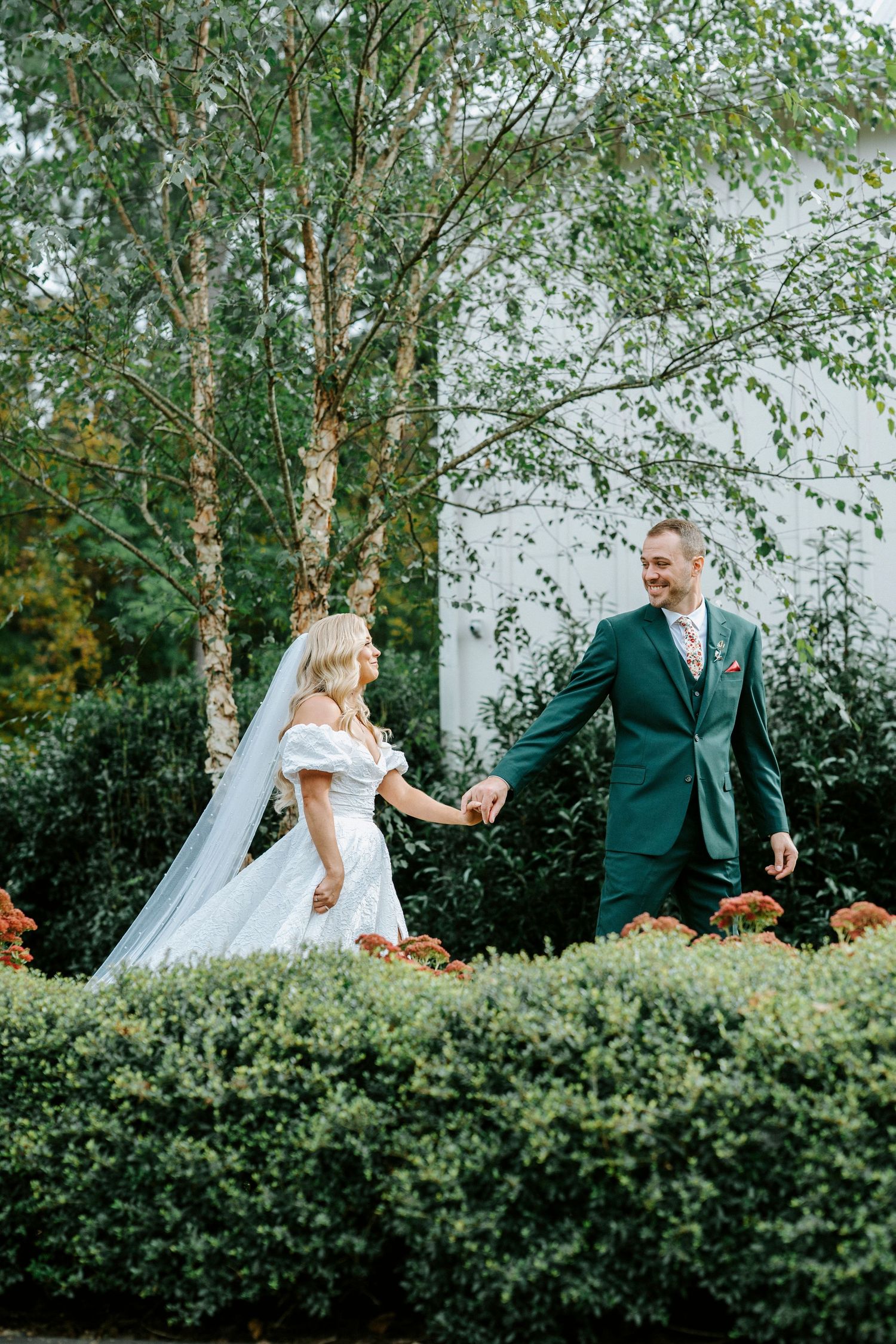 Bride and groom share romantic moments together in a garden setting with birch trees and green hedges in the background.