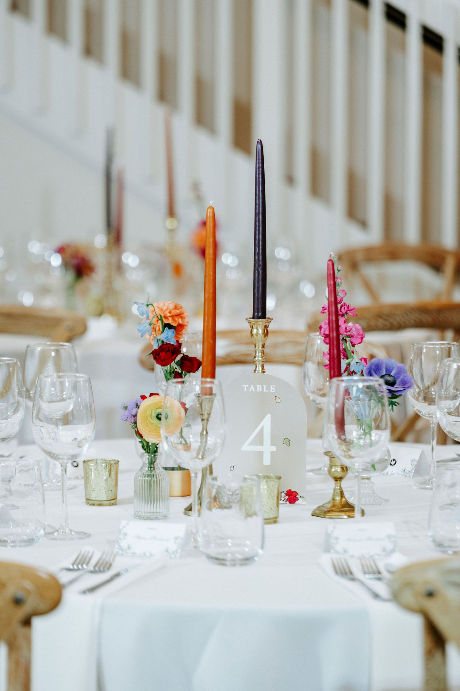 Elegant wedding table setting with colorful taper candles and delicate floral arrangements on crisp white linens.