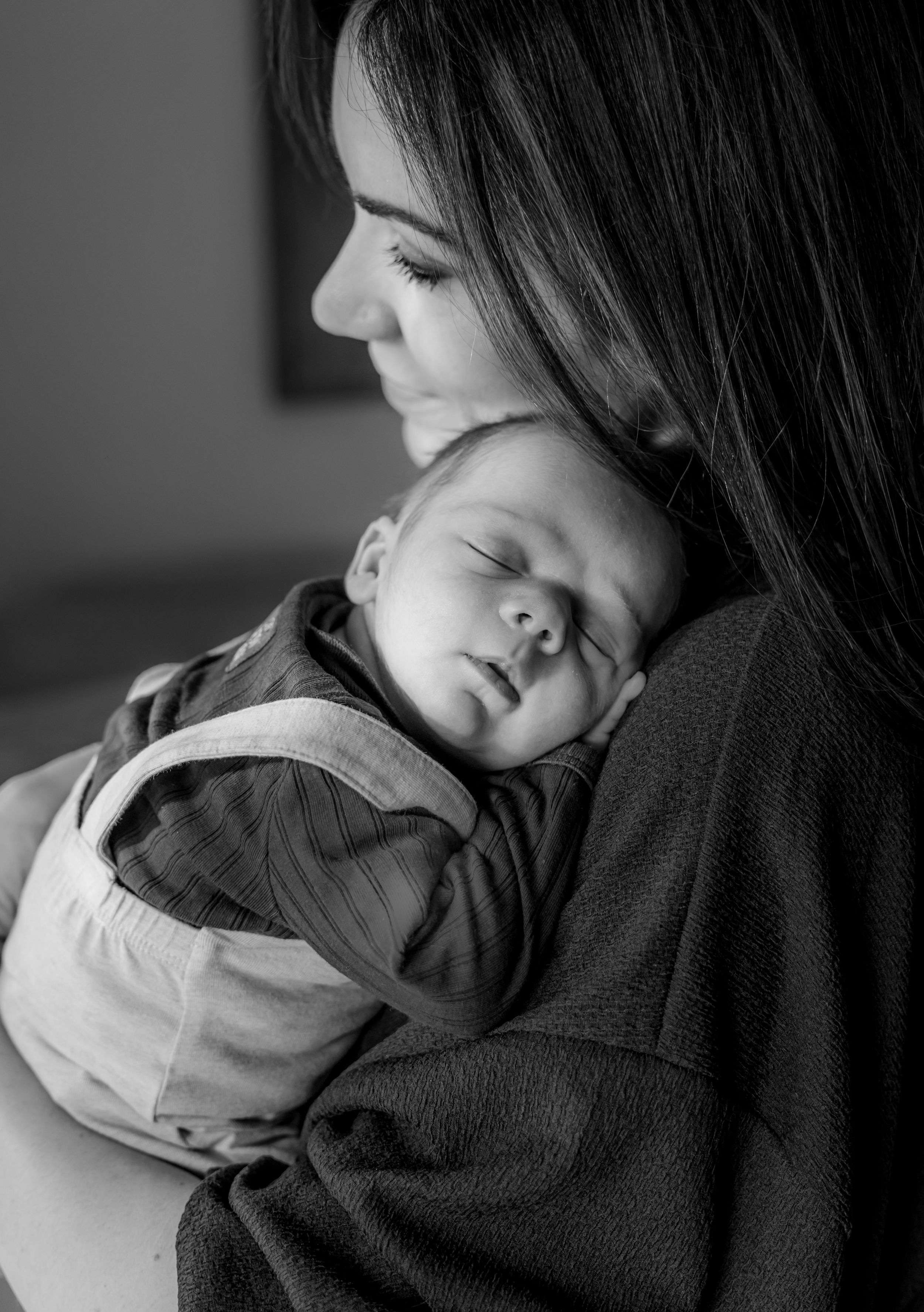 A black and white portrait of a sleeping infant being cradled against someone's chest.
