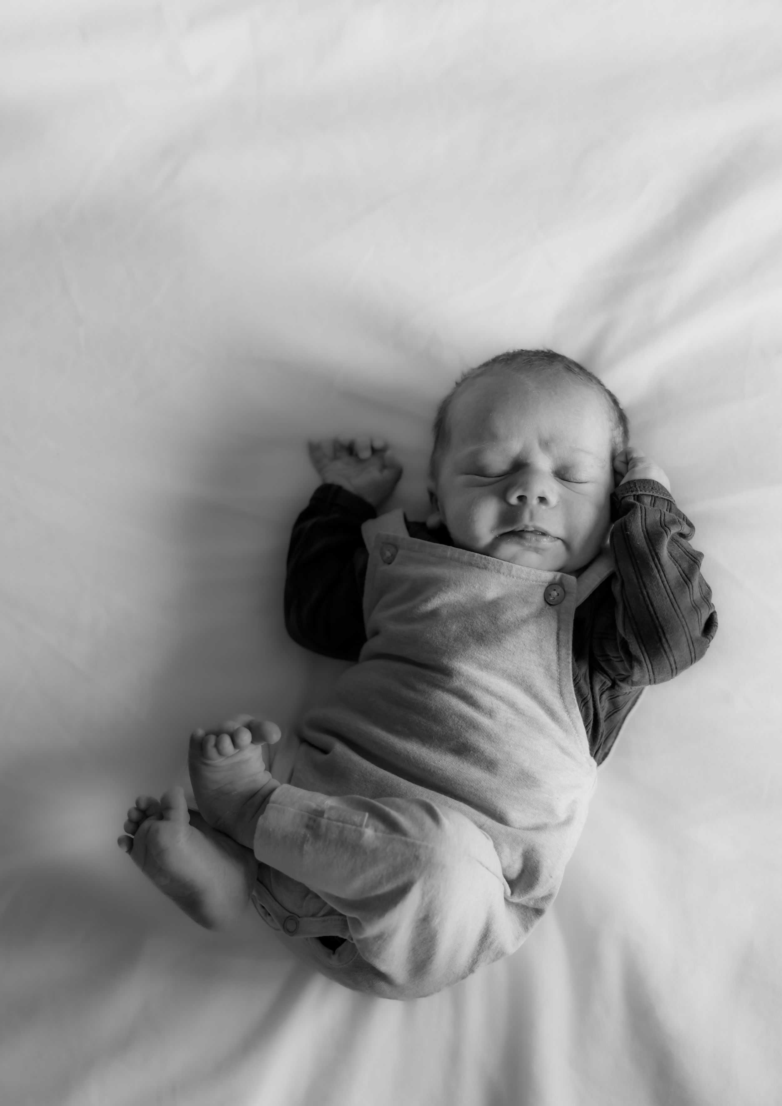 Overhead black and white view of a sleeping newborn baby on white bedding.