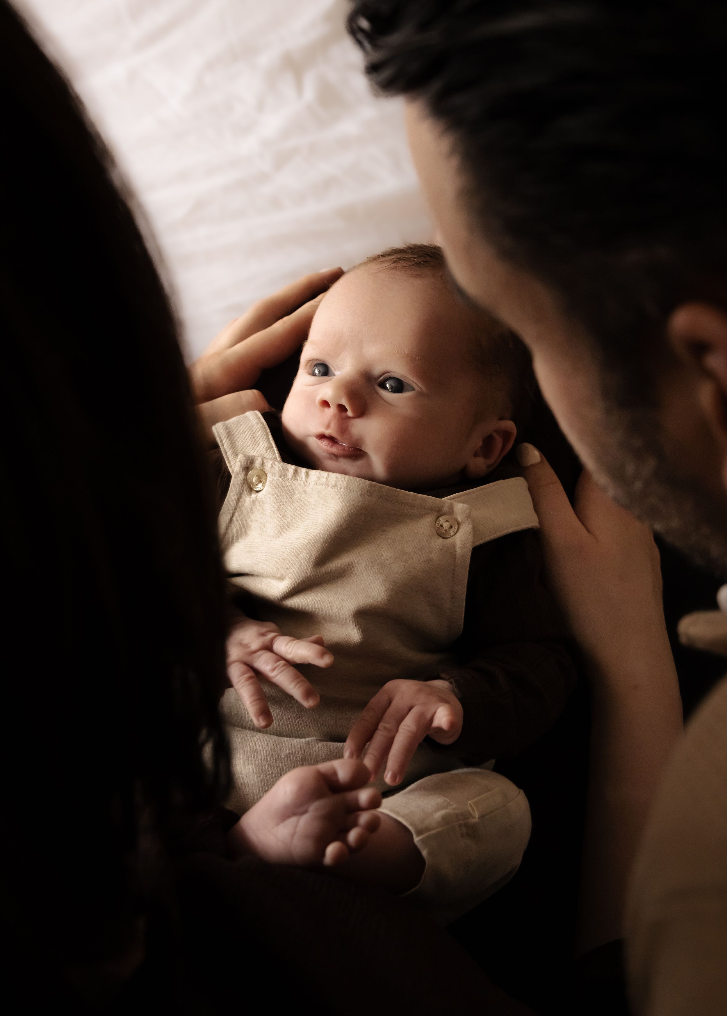 A close-up shot of an alert baby in beige clothing looking up at someone.