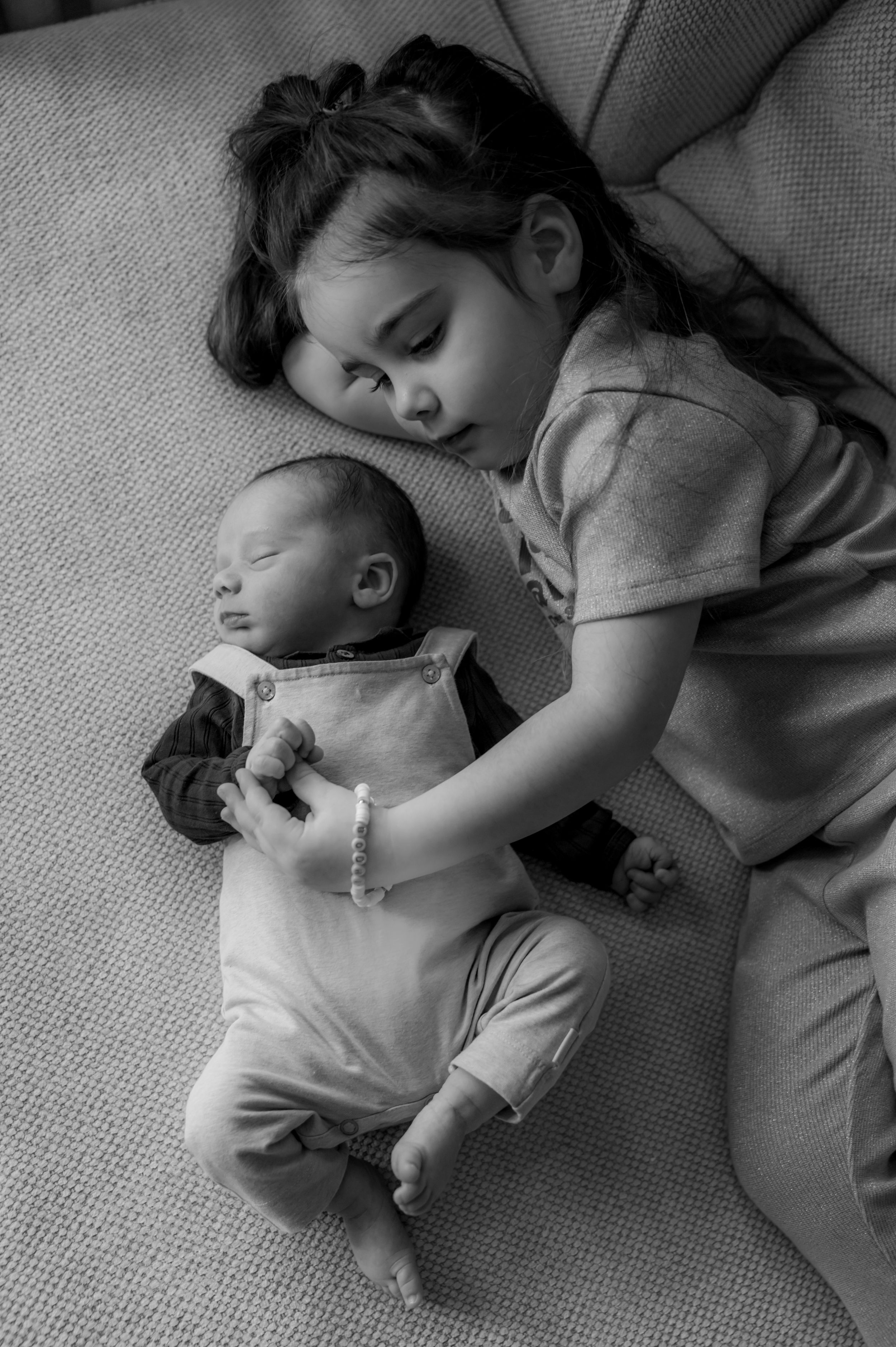 A young child and baby sleeping peacefully together on a couch in black and white.