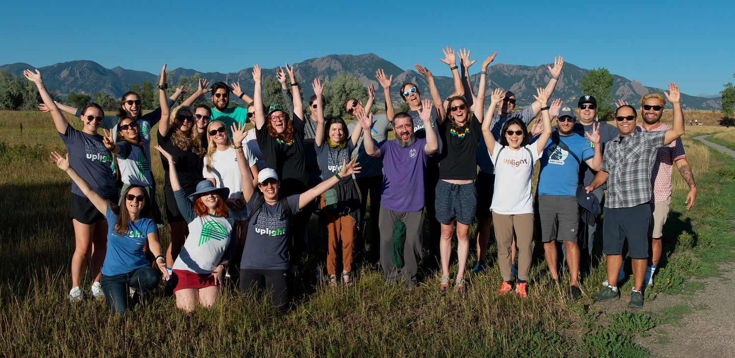 A group of people with raised arms in celebration against a backdrop of the Boulder Flat irons and blue sky.