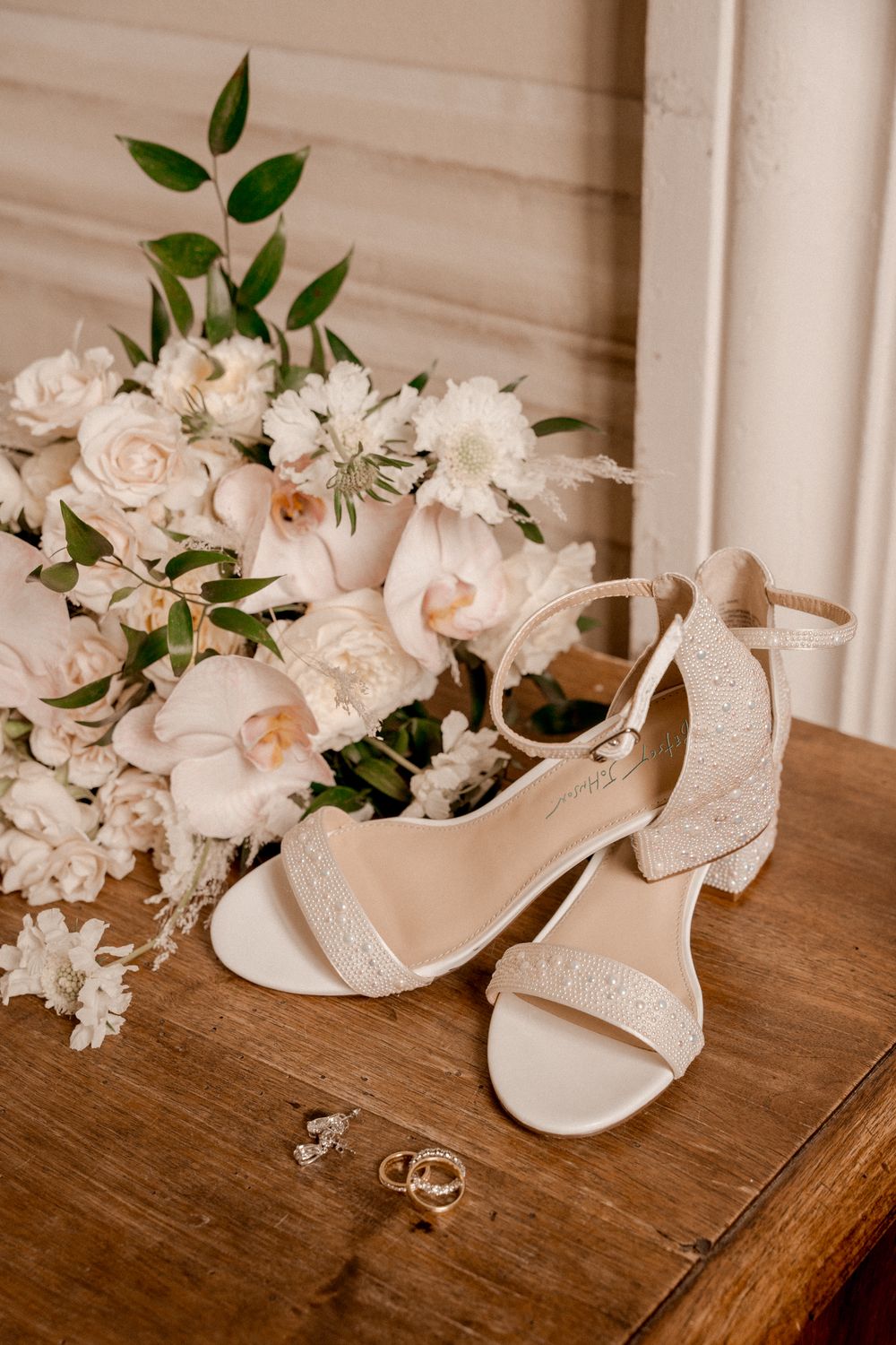 Elegant bridal shoes and white floral arrangements displayed on wooden surface.
