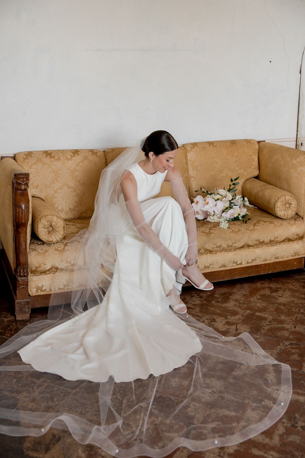 Wedding dress with flowing train arranged on vintage beige couch.