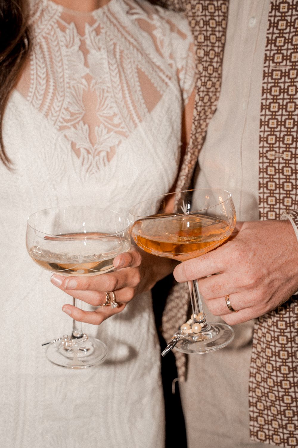 Close-up of hands holding champagne glasses with a decorative patterned wall in the background.