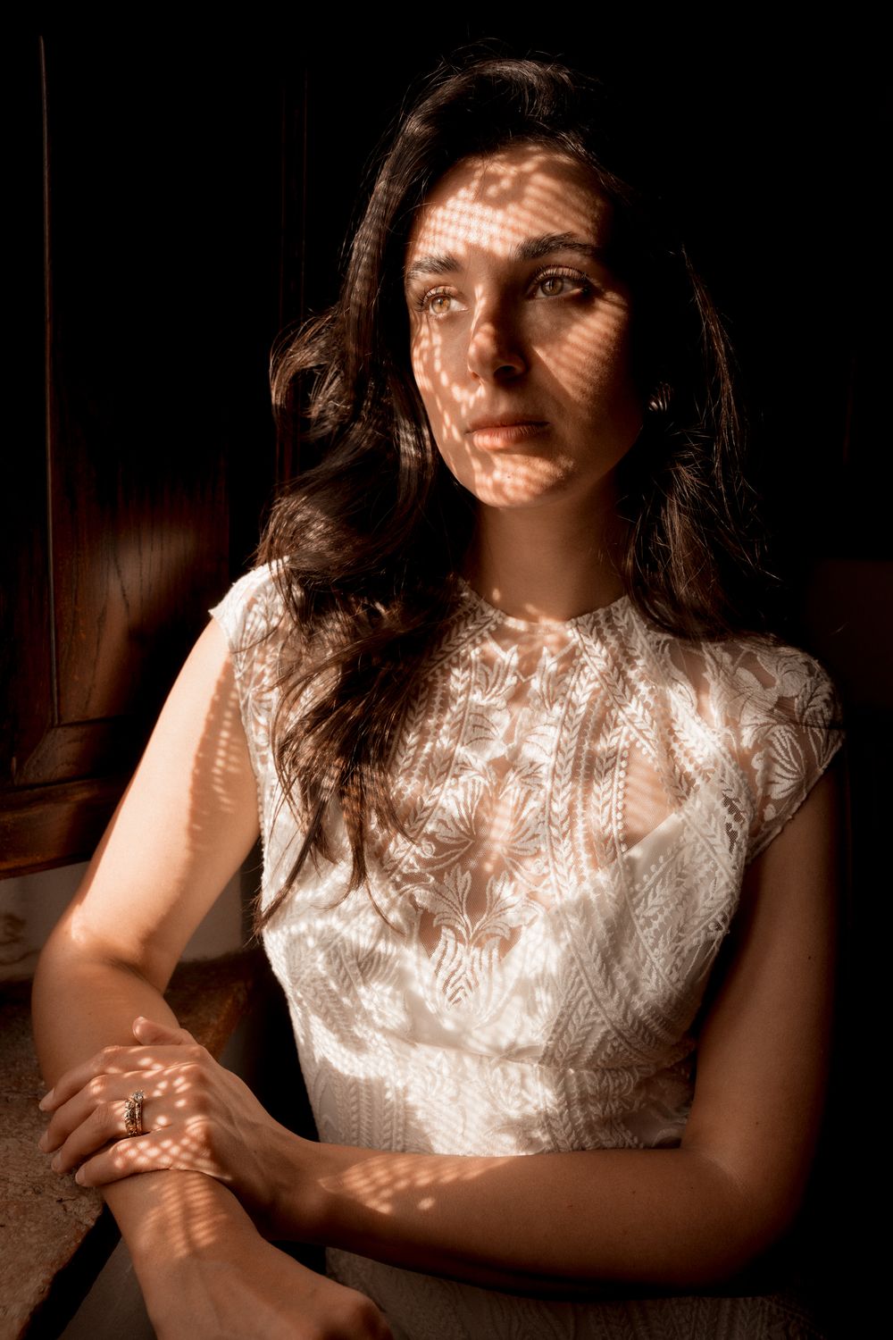 Artistic portrait in dramatic lighting showing a white lace dress detail.