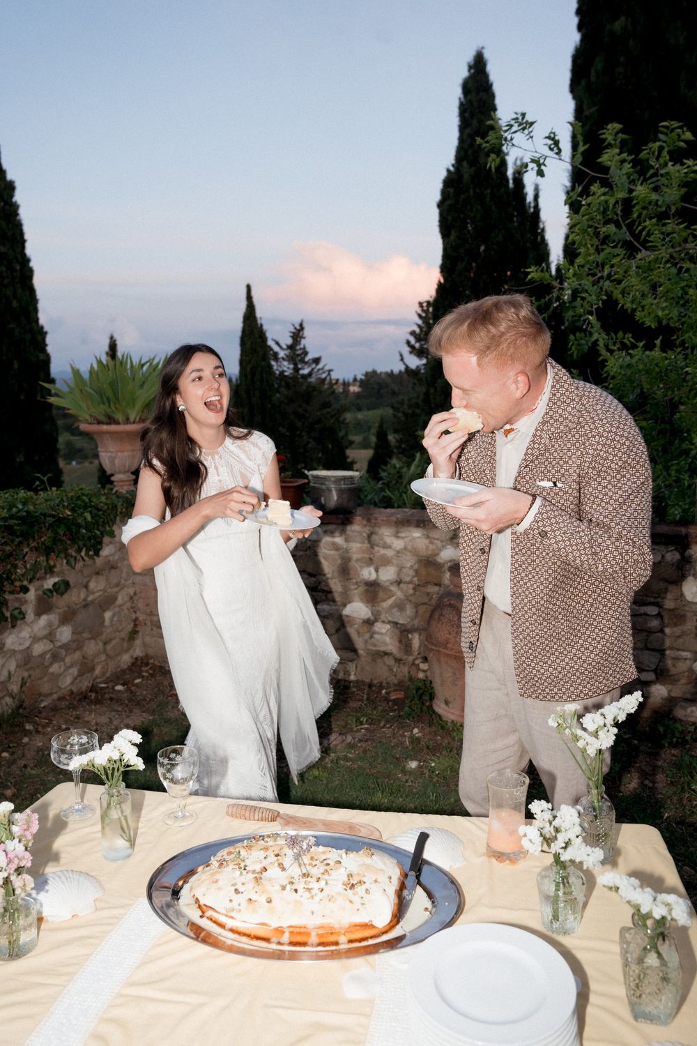 Couple sharing a playful moment while cutting their wedding cake at an outdoor reception.