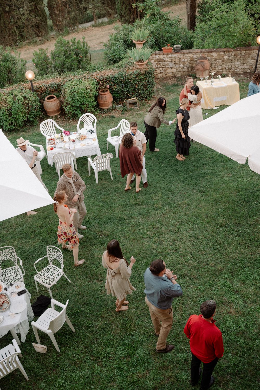 An outdoor garden party with white chairs and tables set up on a lawn surrounded by greenery.