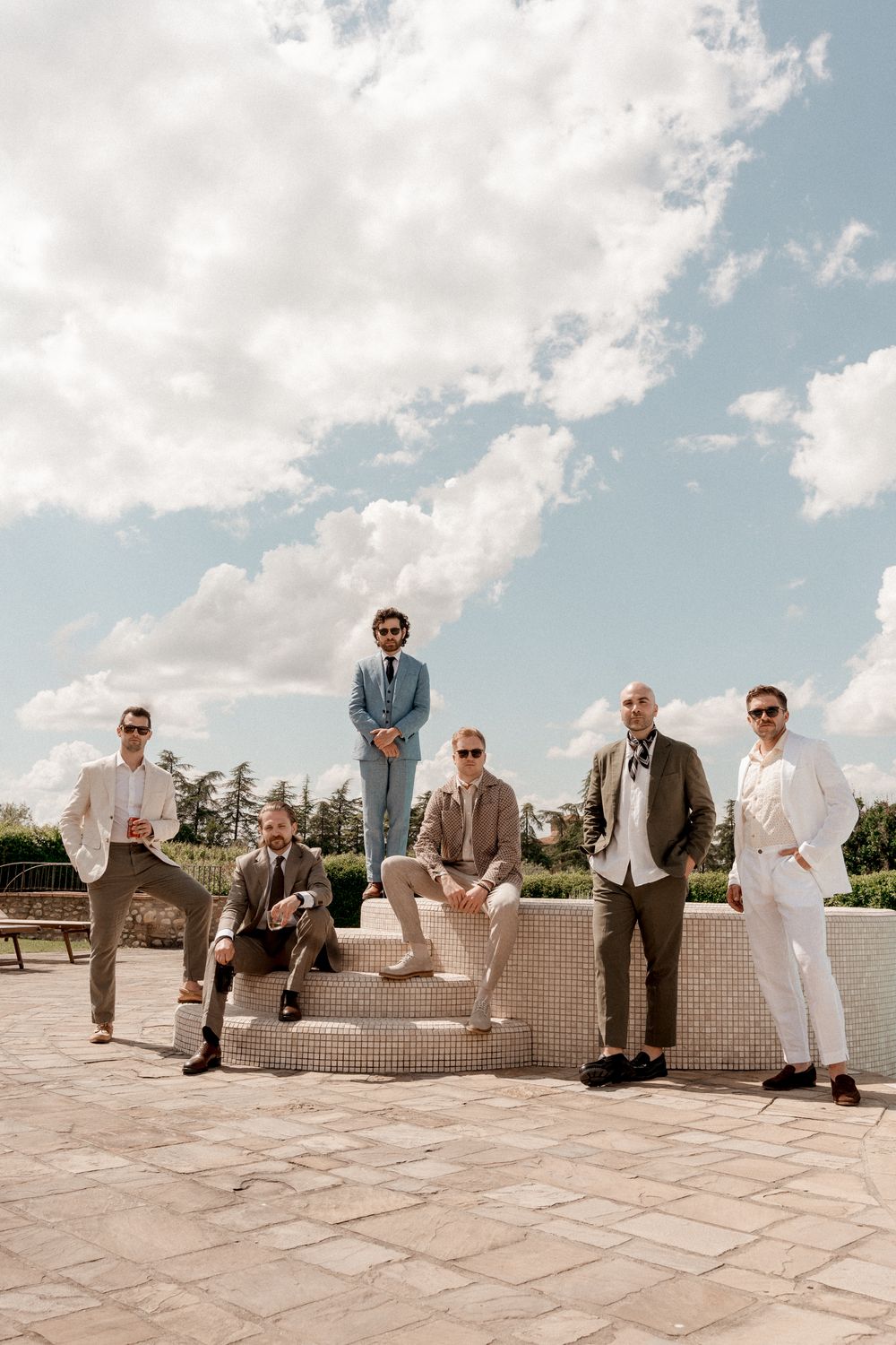 Group in formal attire lounging on white concrete benches under cloudy sky.