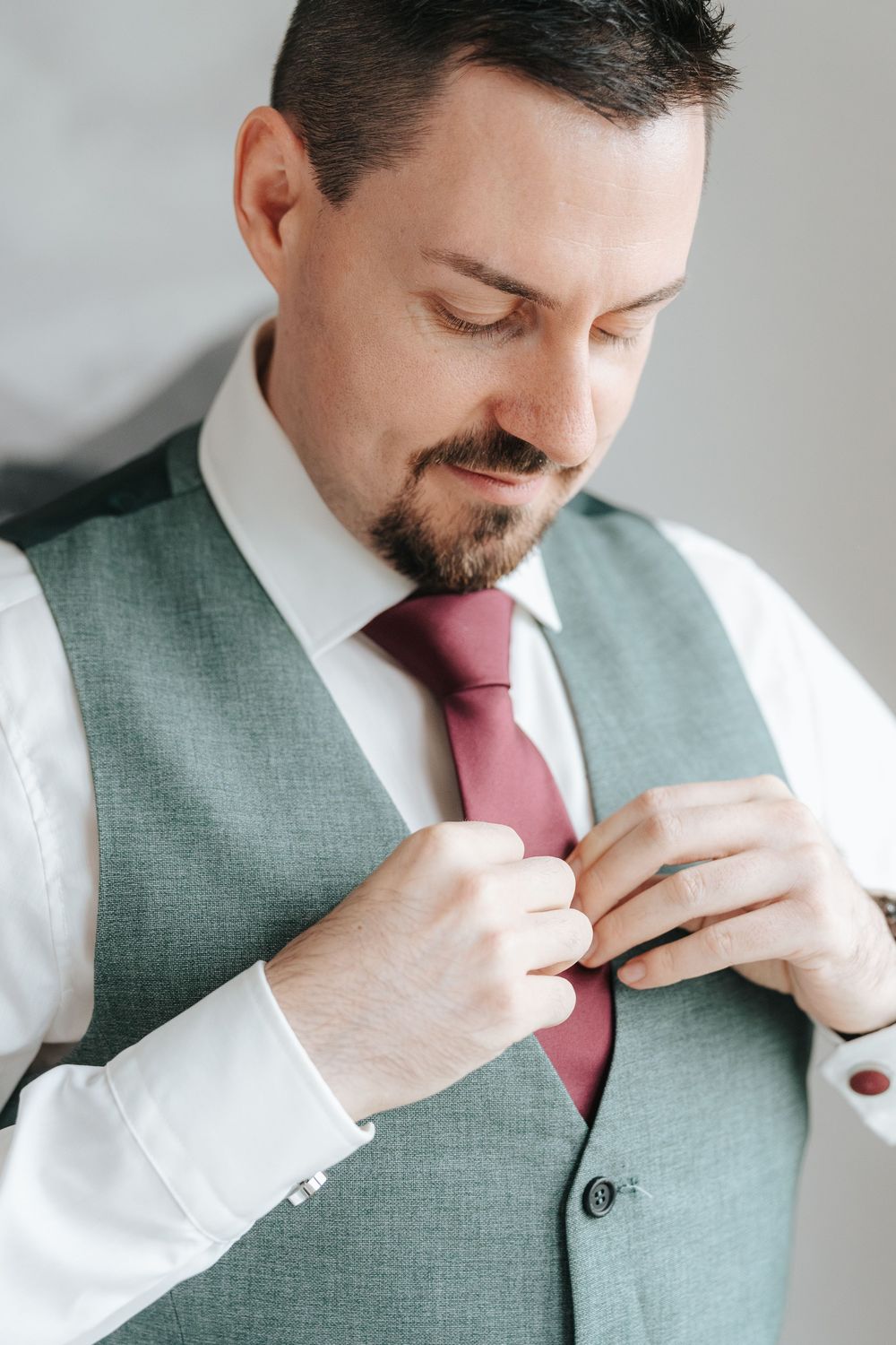 A man in a green vest and pink tie adjusts his collar in a series of professional headshots.