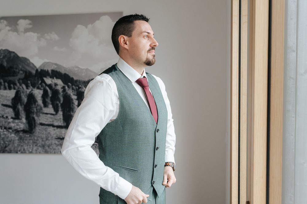A person in a white dress shirt and green vest poses in three different positions against a wooden wall.