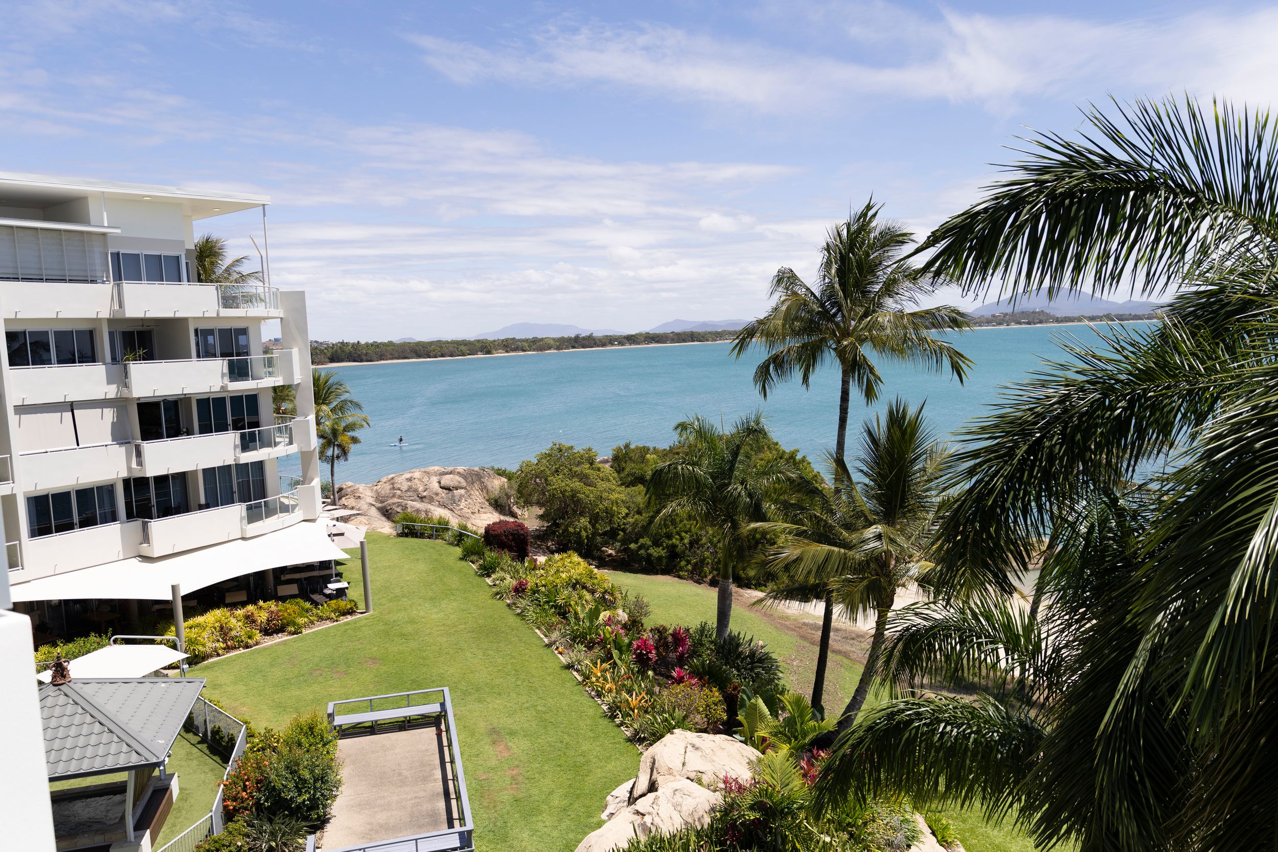 Coastal view from a luxury resort balcony showing palm trees, manicured lawns and turquoise ocean waters.