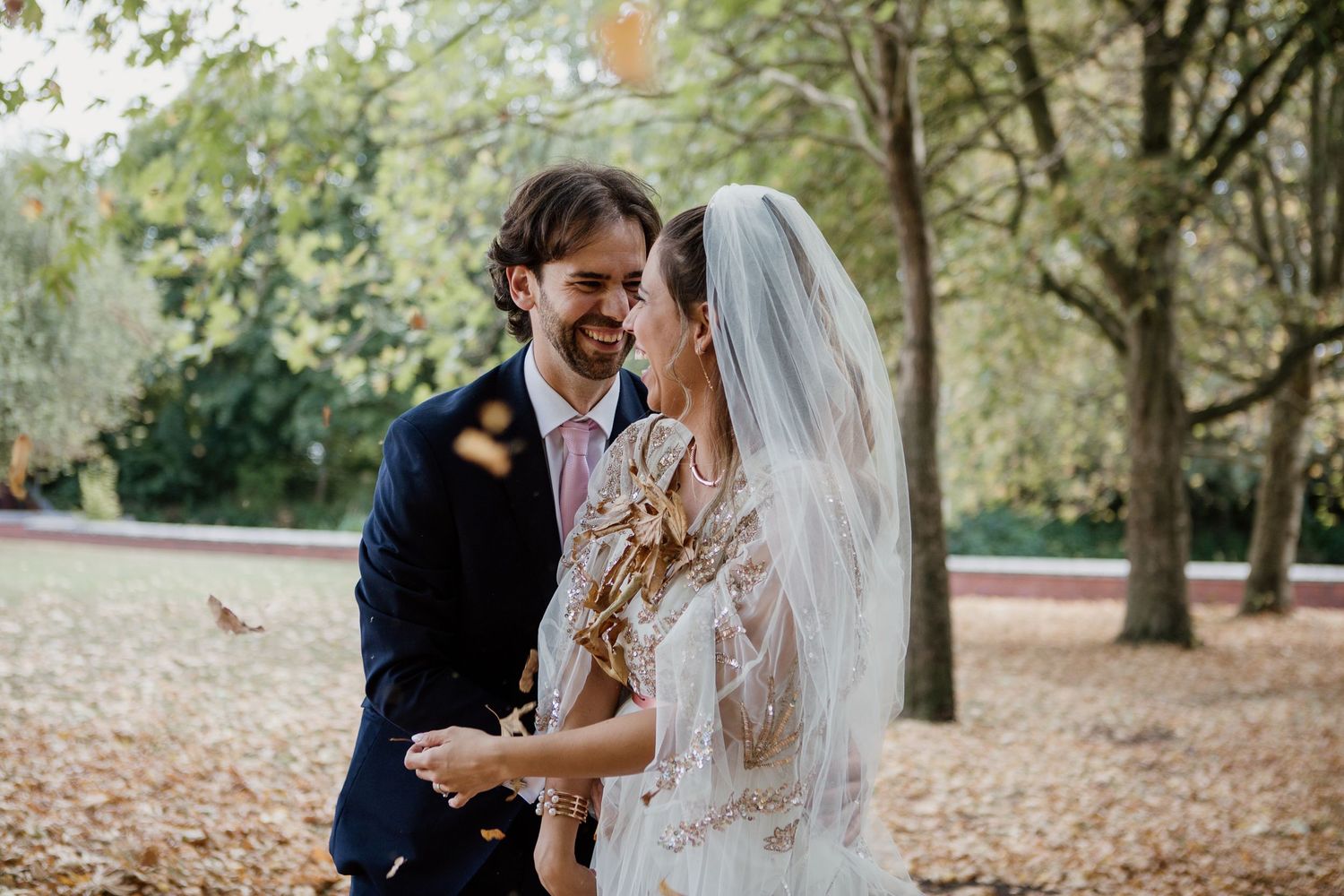 Romantic wedding couple shares tender moments among autumn trees in a park setting.