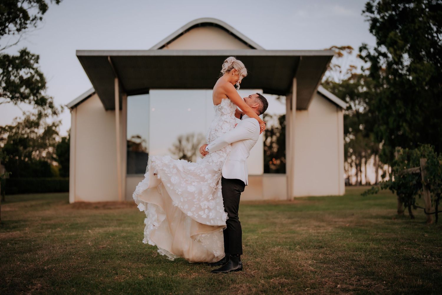 A romantic wedding photoshoot in front of a white building at sunset.