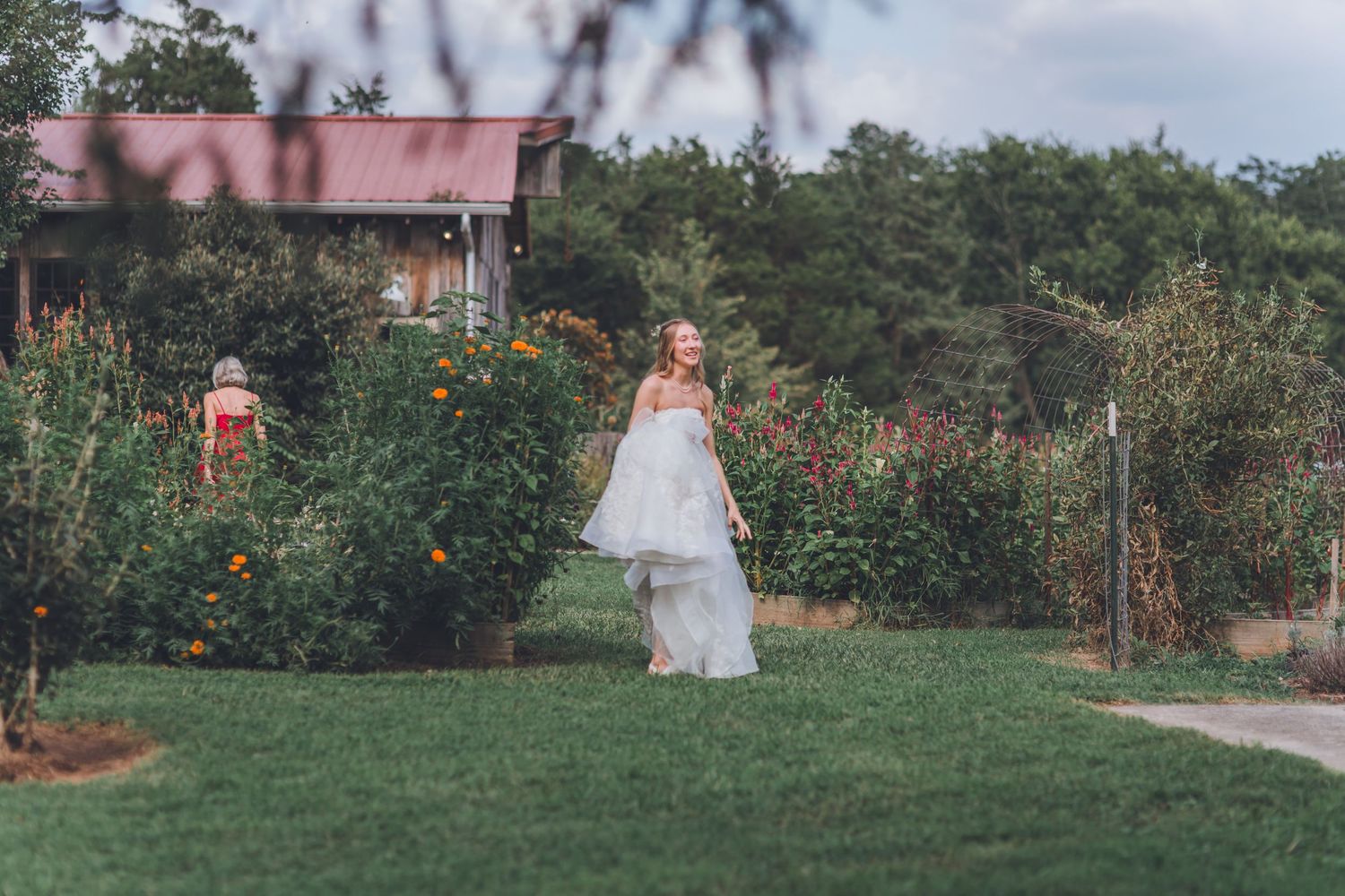 A couple walks hand in hand through a lush garden path surrounded by blooming flowers and greenery.