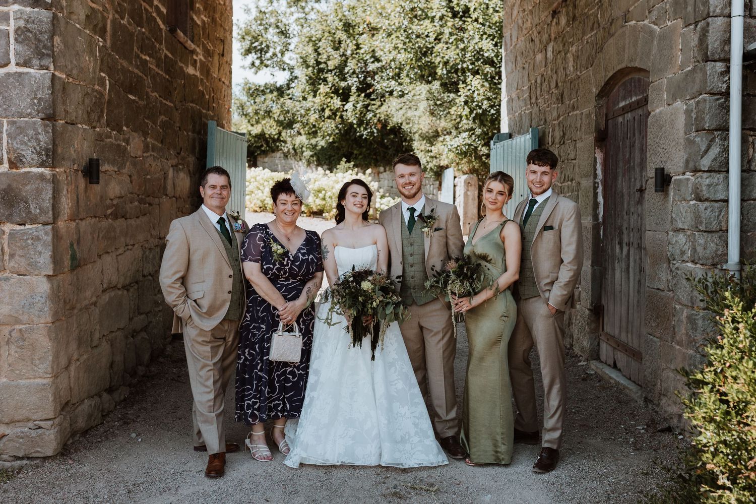 Wedding party poses in a rustic stone archway during an outdoor celebration at The Courtyard Venue, Oswestry.